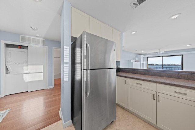 kitchen with dark countertops, visible vents, freestanding refrigerator, and stacked washer and dryer