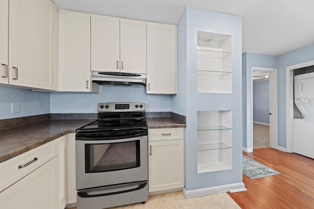 kitchen with stainless steel range with electric cooktop, white cabinets, stacked washer / drying machine, under cabinet range hood, and dark countertops