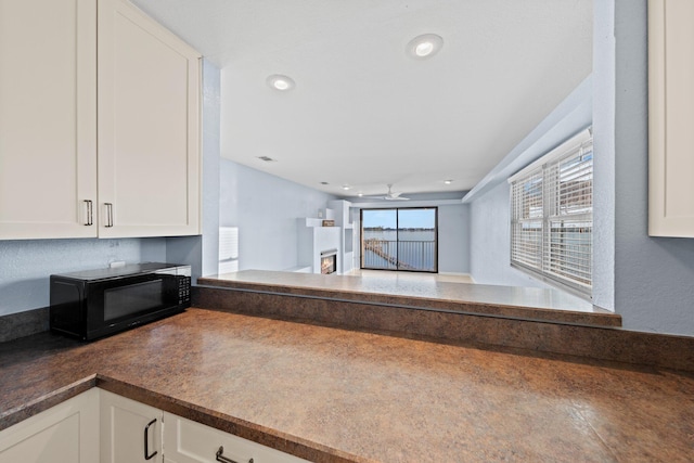 kitchen with dark countertops, a warm lit fireplace, black microwave, and white cabinetry