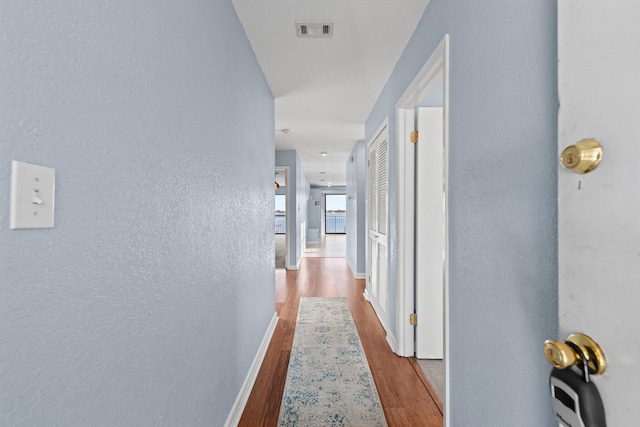 hallway with a textured wall, visible vents, baseboards, and wood finished floors