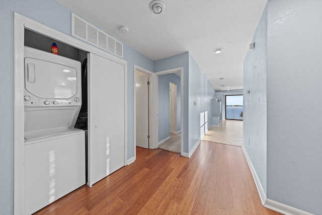 laundry room featuring visible vents, baseboards, laundry area, wood finished floors, and stacked washer / drying machine