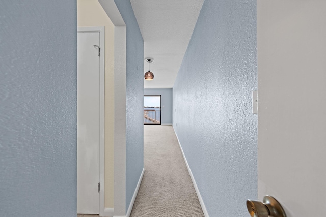 corridor with carpet flooring, a textured wall, and baseboards