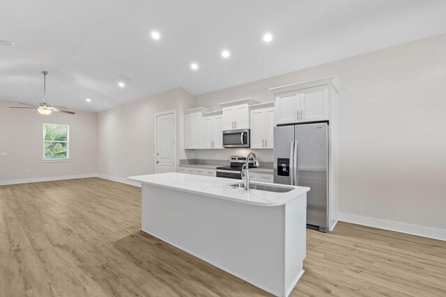 kitchen with appliances with stainless steel finishes, a kitchen island with sink, light wood finished floors, white cabinets, and baseboards