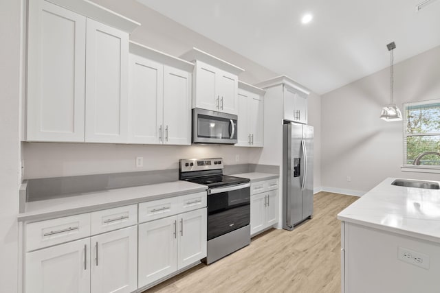 kitchen featuring appliances with stainless steel finishes, a sink, white cabinetry, pendant lighting, and vaulted ceiling