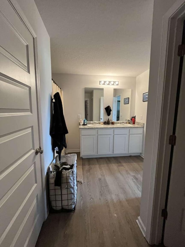 bathroom featuring a sink, a textured ceiling, wood finished floors, double vanity, and baseboards