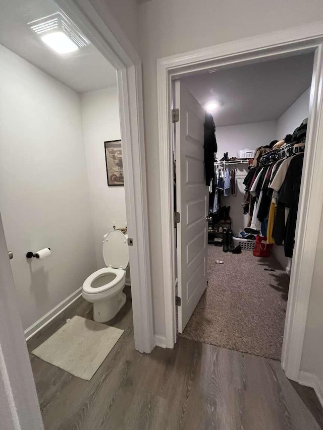 bathroom featuring a walk in closet, baseboards, toilet, and wood finished floors