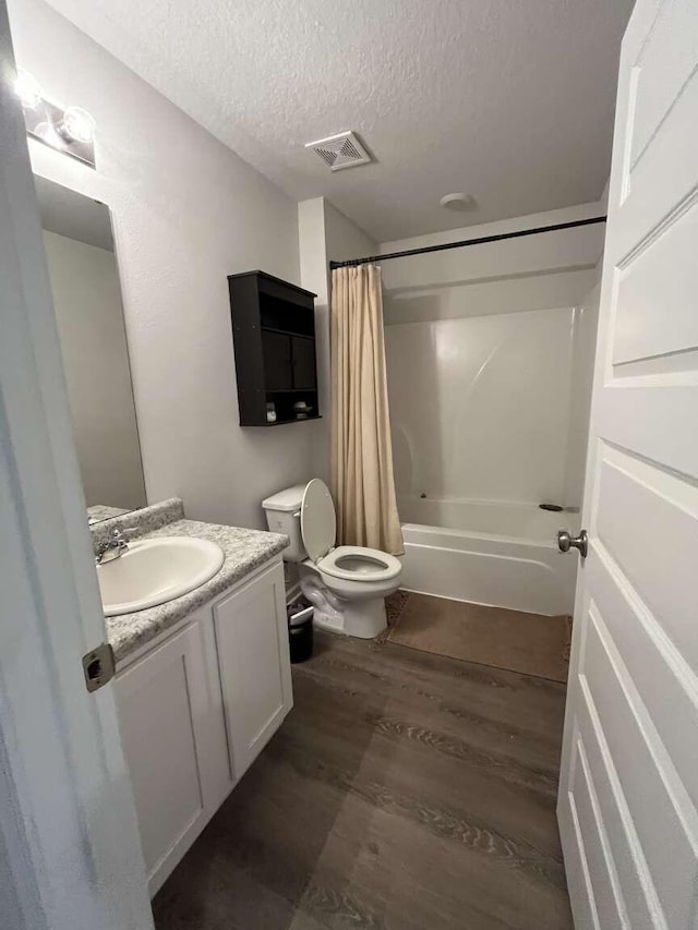 bathroom featuring vanity, wood finished floors, visible vents, shower / bath combination with curtain, and a textured ceiling