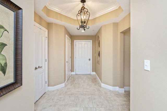 hall with a tray ceiling, baseboards, an inviting chandelier, and ornamental molding