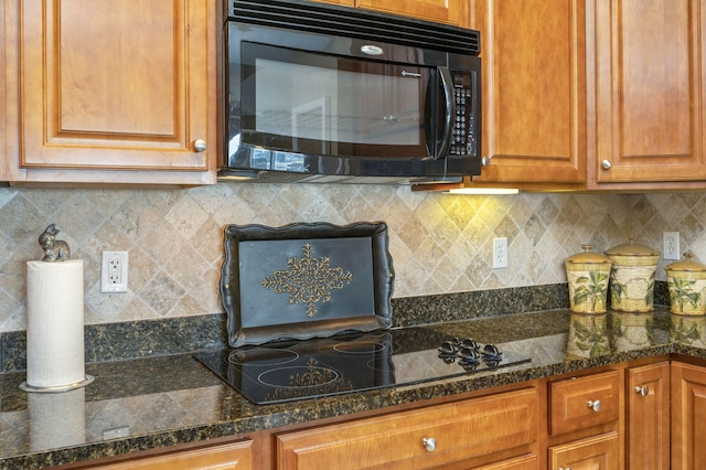 kitchen featuring decorative backsplash, brown cabinets, black appliances, and dark stone countertops