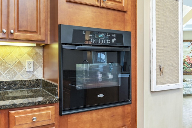 kitchen featuring brown cabinetry, dobule oven black, tasteful backsplash, and dark stone counters