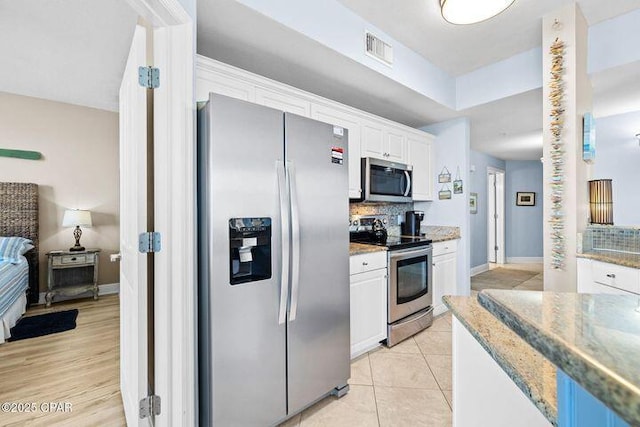 kitchen with visible vents, backsplash, white cabinetry, appliances with stainless steel finishes, and light tile patterned floors