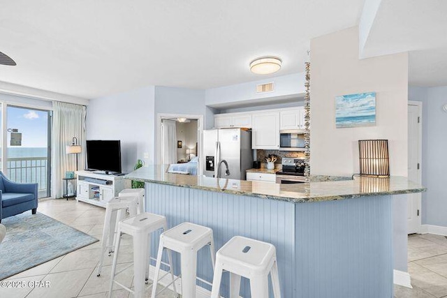 kitchen featuring backsplash, white cabinetry, stainless steel appliances, light tile patterned flooring, and light stone countertops