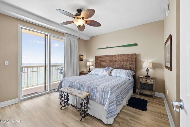 bedroom with baseboards, wood finished floors, a water view, and access to outside