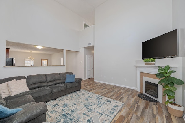 living room featuring wood finished floors, baseboards, a towering ceiling, a glass covered fireplace, and a chandelier