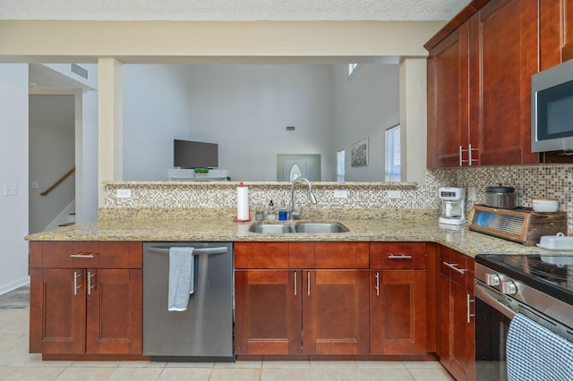 kitchen featuring light stone countertops, decorative backsplash, a peninsula, stainless steel appliances, and a sink