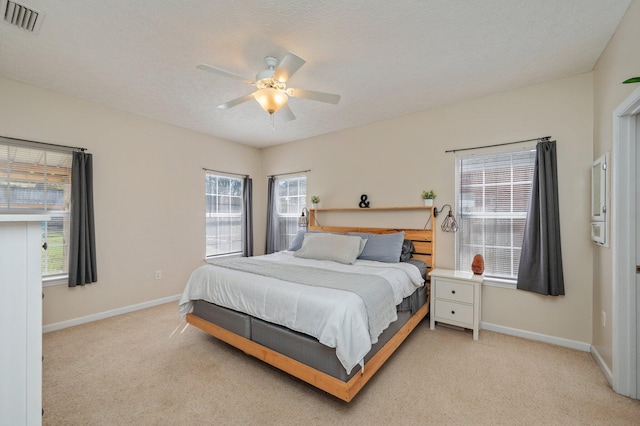 bedroom with visible vents, light carpet, a textured ceiling, baseboards, and ceiling fan