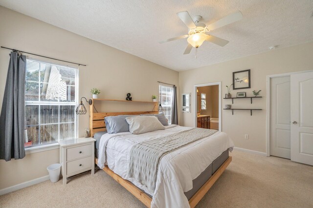 bedroom with a ceiling fan, baseboards, ensuite bathroom, a textured ceiling, and light colored carpet