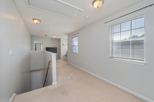 hallway with baseboards, light colored carpet, attic access, an upstairs landing, and a textured ceiling