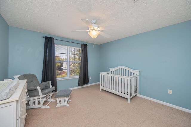 bedroom with a nursery area, light colored carpet, a ceiling fan, and baseboards