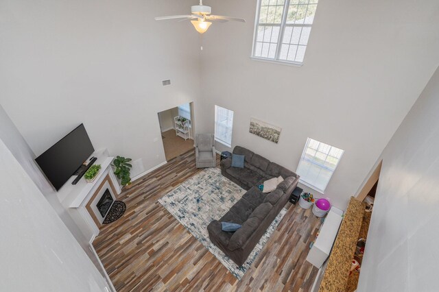 living area featuring visible vents, a ceiling fan, wood finished floors, a high ceiling, and baseboards