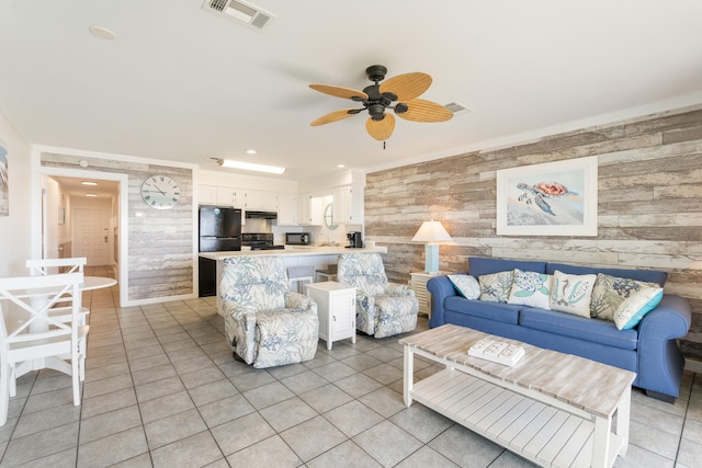 living room with light tile patterned floors, visible vents, wood walls, and a ceiling fan