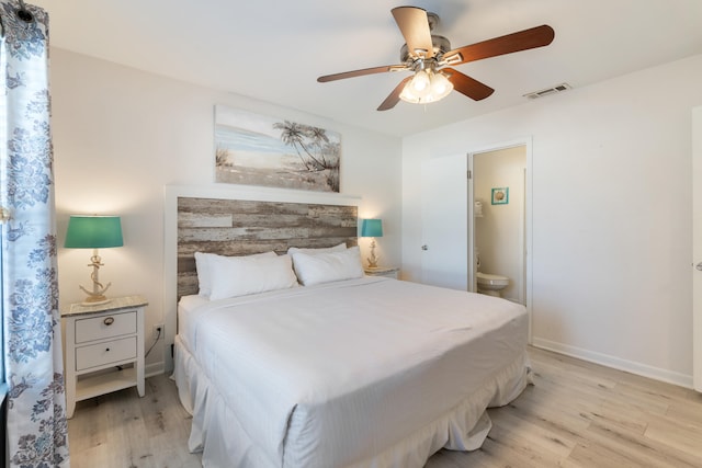 bedroom featuring light wood finished floors, visible vents, ceiling fan, baseboards, and ensuite bath