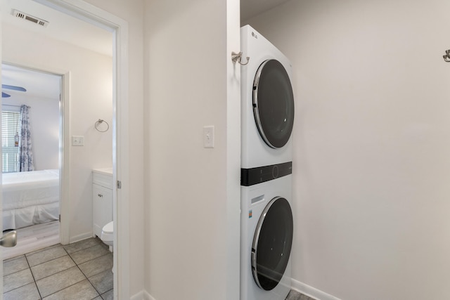 clothes washing area with visible vents, light tile patterned floors, stacked washer / drying machine, baseboards, and laundry area