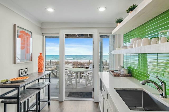 kitchen featuring ornamental molding, a beach view, a sink, wood finished floors, and white cabinetry