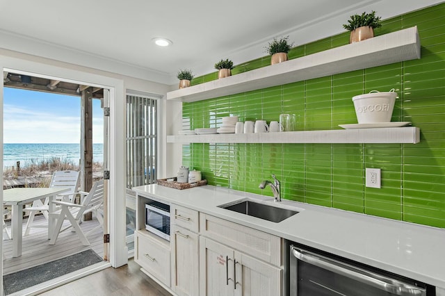 kitchen with wood finished floors, a sink, a water view, appliances with stainless steel finishes, and backsplash