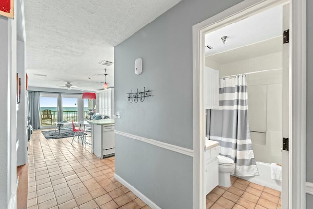 hallway featuring light tile patterned flooring, visible vents, a textured ceiling, and baseboards