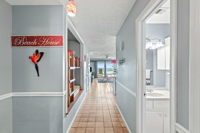 hallway featuring light tile patterned floors, baseboards, visible vents, a sink, and a textured ceiling