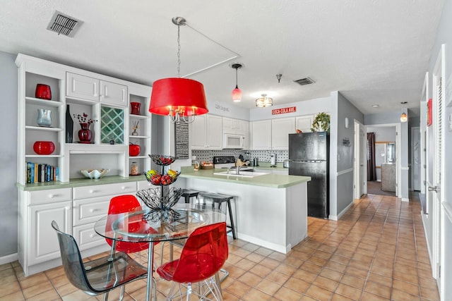 kitchen with white cabinetry, white microwave, visible vents, and freestanding refrigerator