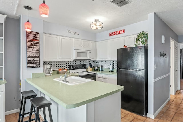 kitchen with white microwave, visible vents, a peninsula, electric range, and freestanding refrigerator