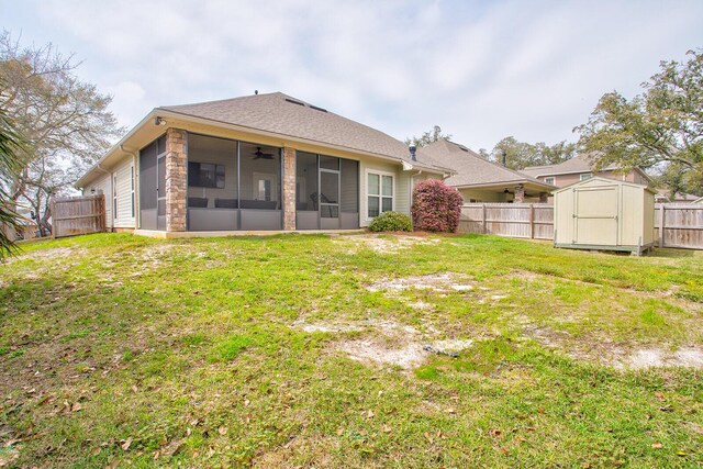 rear view of house featuring a storage unit, a fenced backyard, a yard, an outdoor structure, and a sunroom
