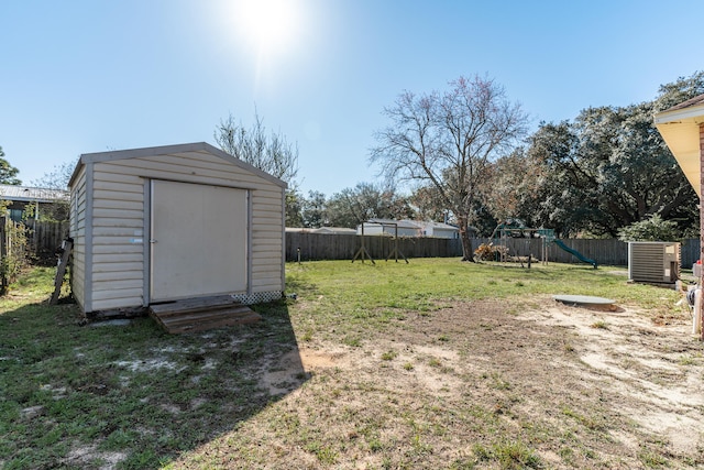 view of yard featuring central AC unit, a fenced backyard, an outdoor structure, a storage shed, and a playground