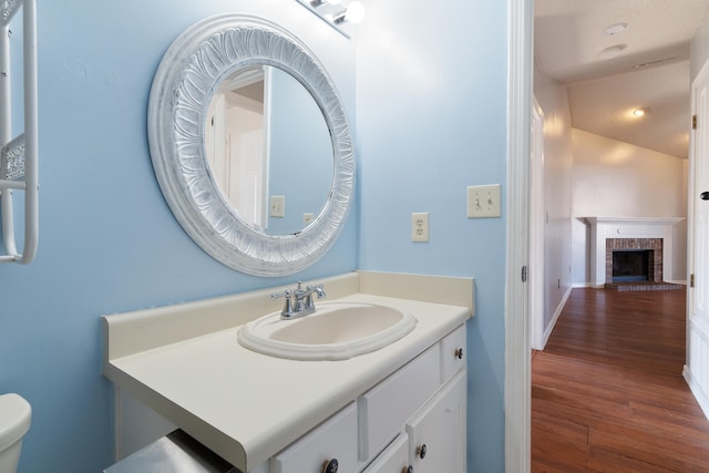 half bath with toilet, a brick fireplace, wood finished floors, and vanity