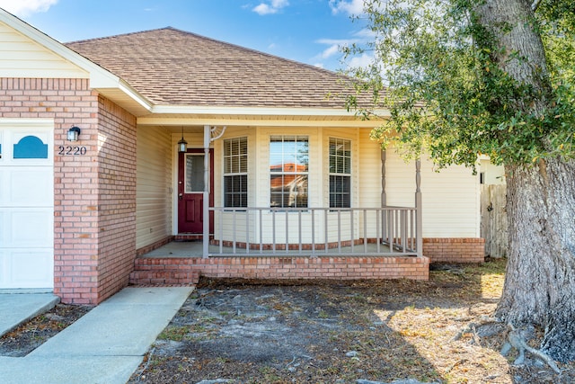 doorway to property with roof with shingles, a porch, and an attached garage