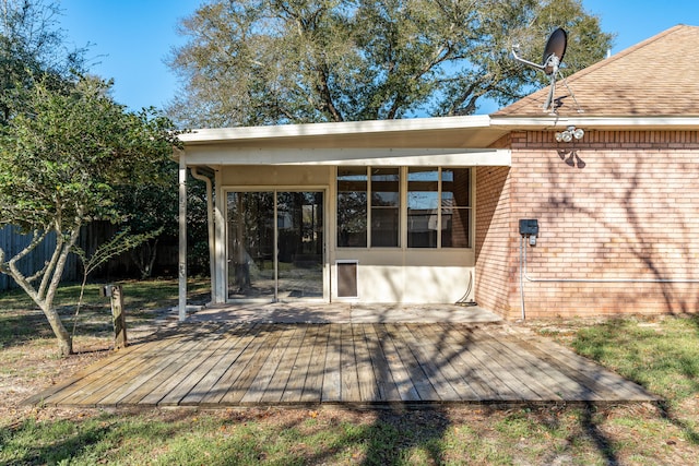 rear view of property featuring brick siding, a sunroom, a deck, and fence