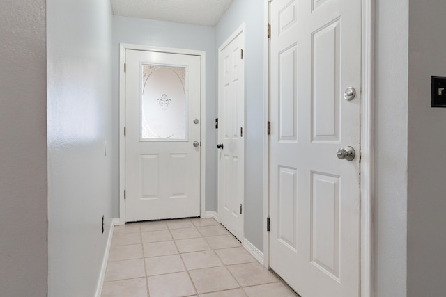 doorway featuring light tile patterned floors, a textured ceiling, and baseboards