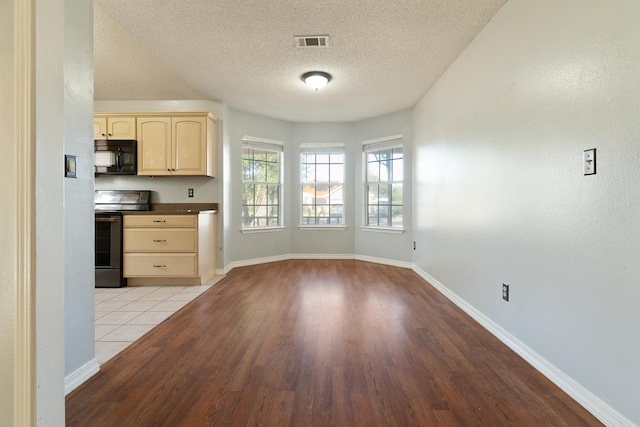 kitchen with visible vents, light brown cabinetry, electric stove, dark countertops, and black microwave