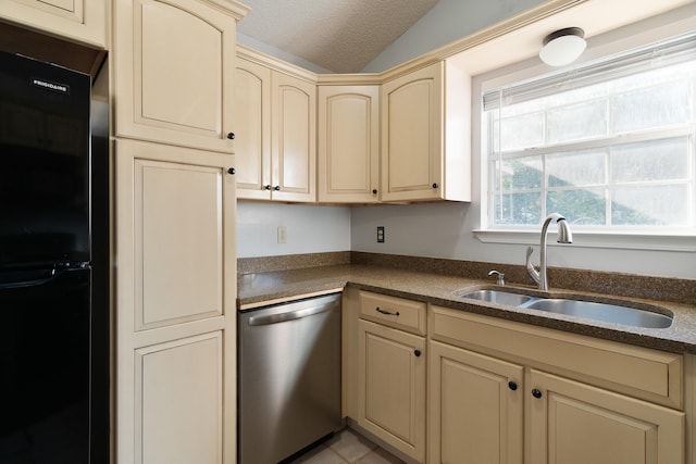 kitchen featuring dark countertops, dishwasher, freestanding refrigerator, cream cabinetry, and a sink