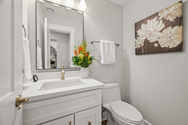 bathroom featuring visible vents, toilet, vanity, and a textured wall