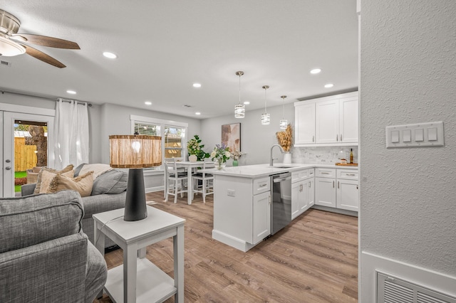 kitchen with white cabinetry, a peninsula, a sink, light wood-style floors, and stainless steel dishwasher