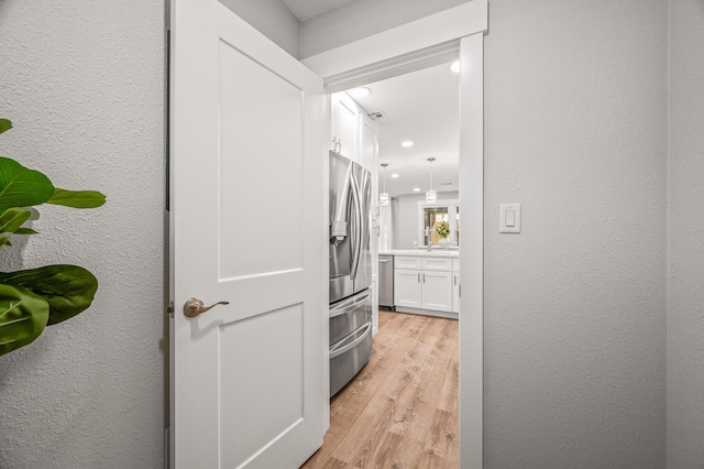 hallway with light wood-style floors, visible vents, and a textured wall