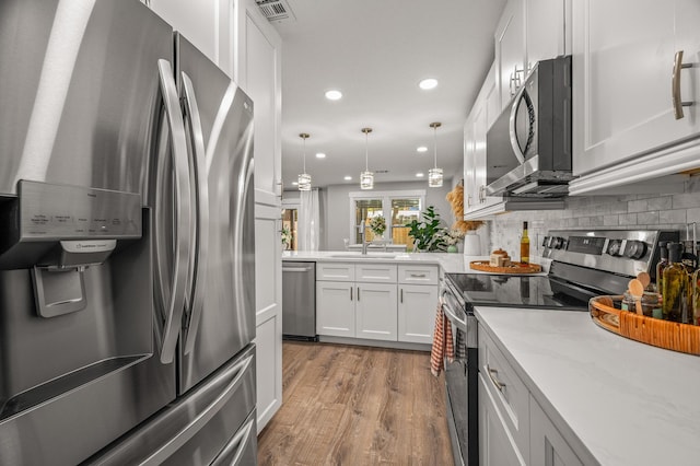 kitchen with light wood-style flooring, a sink, stainless steel appliances, white cabinetry, and backsplash