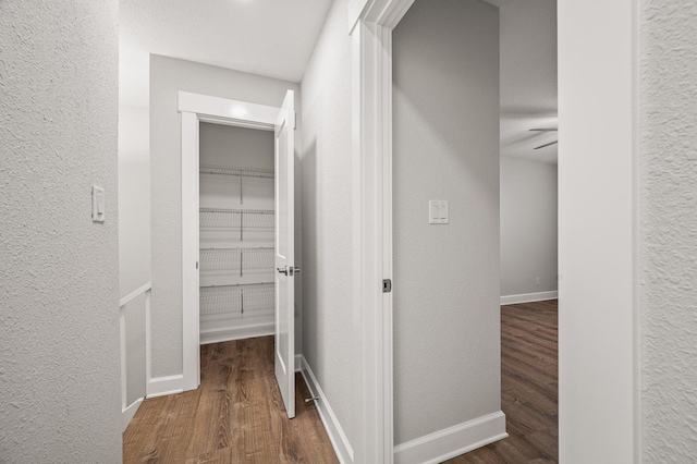 hall featuring baseboards, wood finished floors, and a textured wall