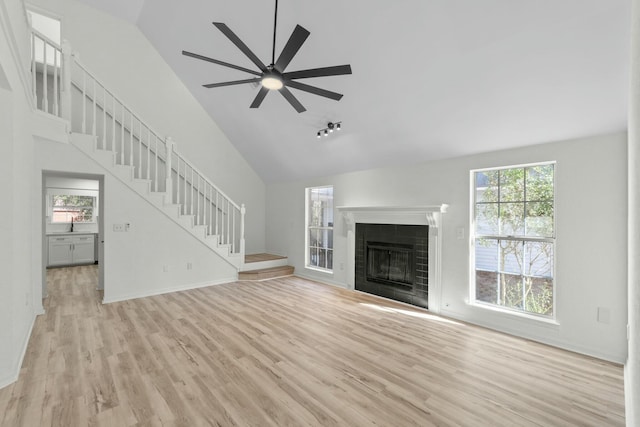 unfurnished living room with high vaulted ceiling, light wood-type flooring, and stairs