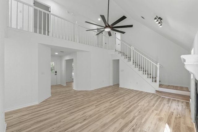 unfurnished living room with stairway, a towering ceiling, a ceiling fan, and wood finished floors