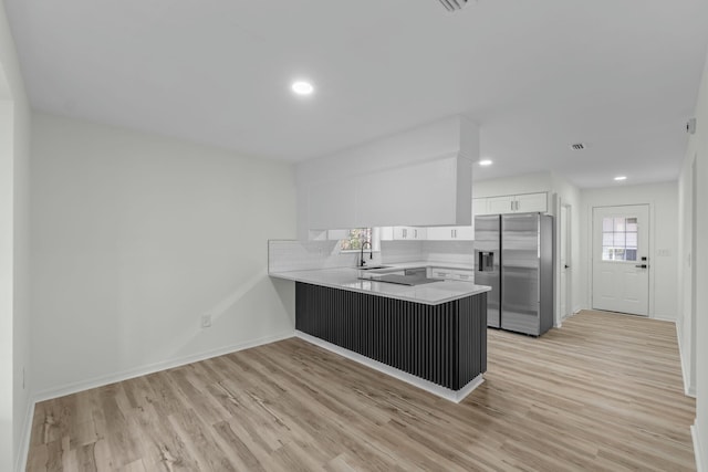 kitchen with a peninsula, stainless steel fridge with ice dispenser, light wood-style floors, and light countertops