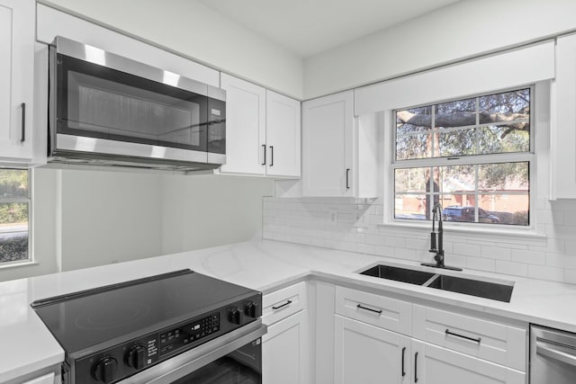 kitchen with decorative backsplash, white cabinetry, appliances with stainless steel finishes, and a sink